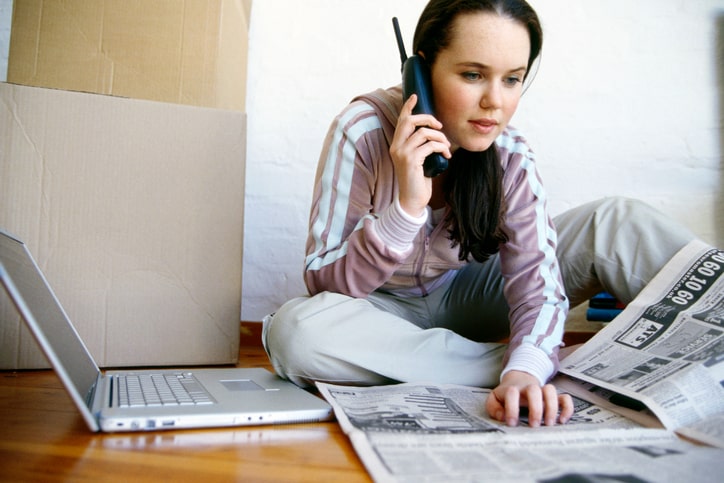 Young woman searching for a house in the newspaper, making a phone call with her mobile phone